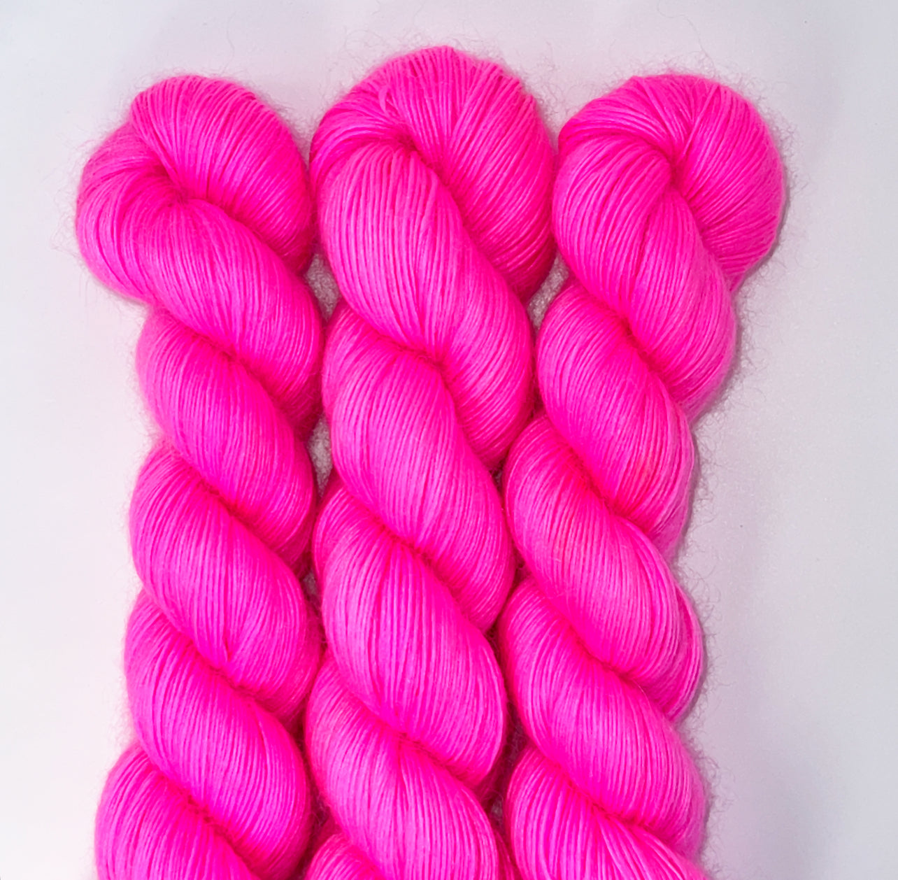 Three skeins of bright pink yarn on a white background
