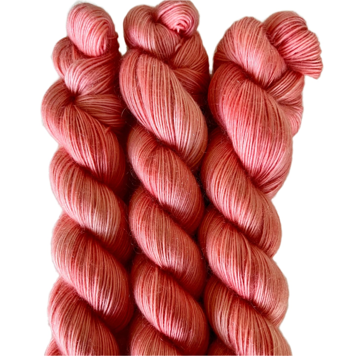 Three skeins of light pink/orange colour yarn on a white background